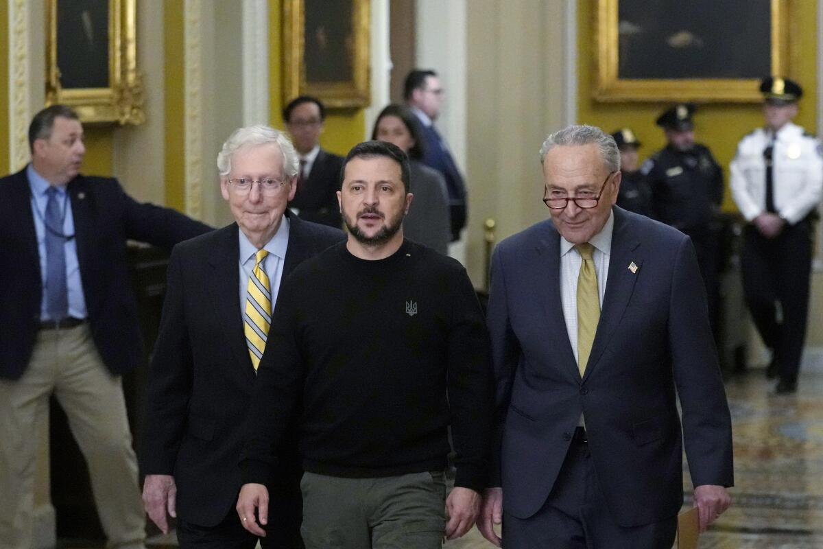 Ukrainian President Volodymyr Zelensky and Sens. Mitch McConnell and Charles E. Schumer walk through a building. 
