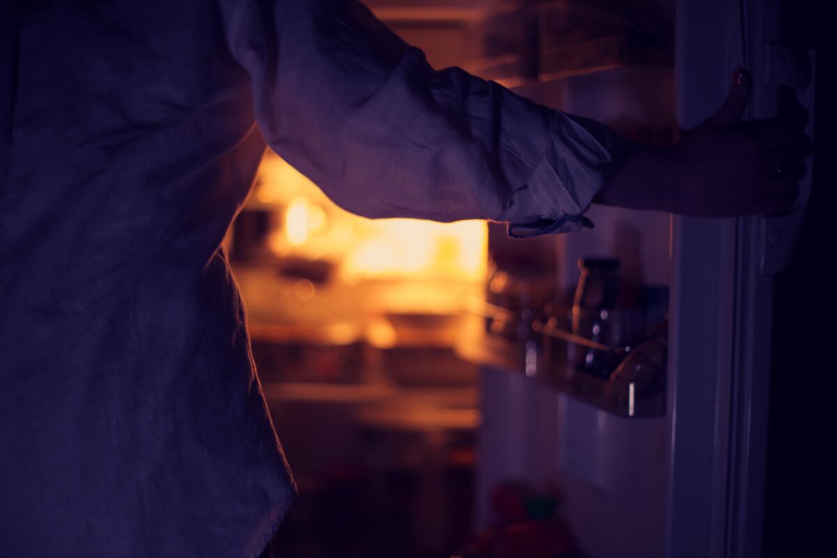 Woman holding refrigerator door open at night