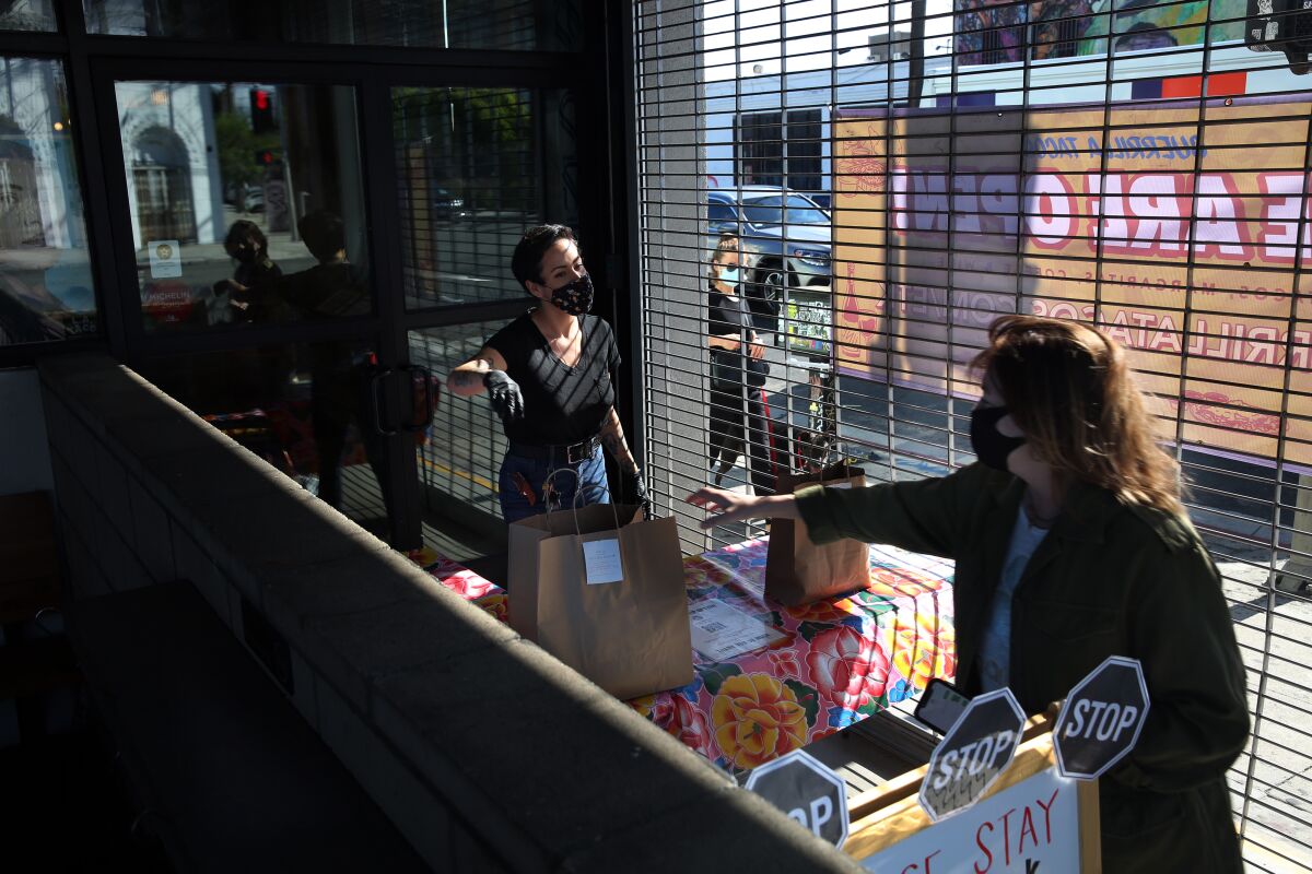 Gretel Diaz, left, hands over a no-contact to-go order for a customer at Guerrilla Tacos