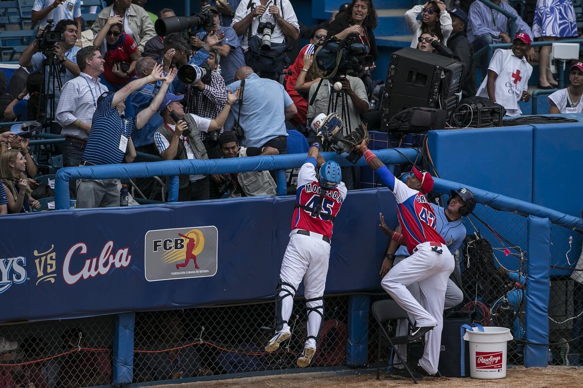 Cuban players can't reach a ball as it falls into the stands during the exhibition baseball game with MLB's Tampa Rays at Estadio Latinoaericano.