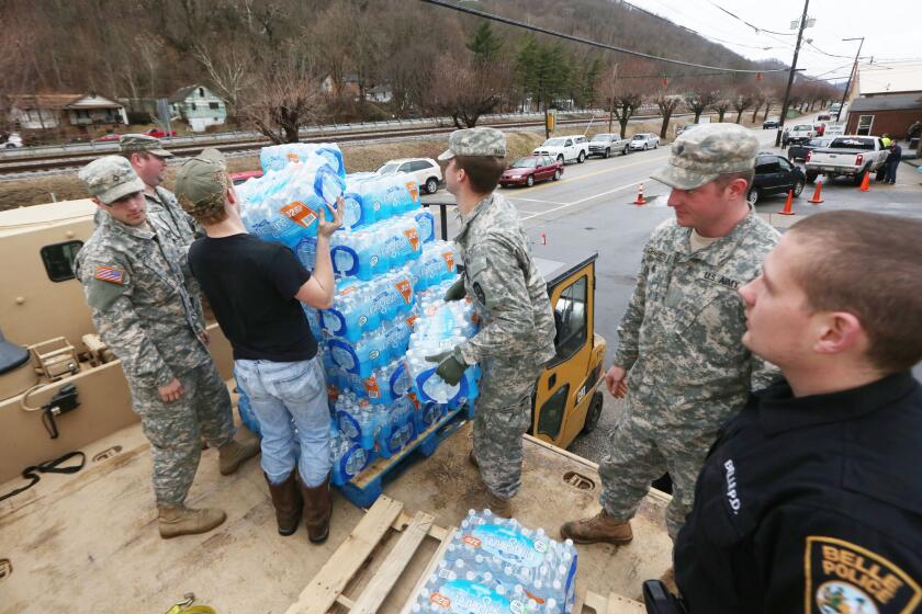 Members of the West Virginia Army National Guard, with a member of the Belle Police Department and a volunteer, offload emergency bottled water from a military truck to a forklift for distribution at the Belle Fire Department on Saturday, Jan. 11.