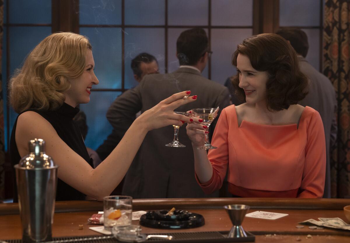 Two women at a bar toast each other with martini glasses in a scene from "The Marvelous Mrs. Maisel."