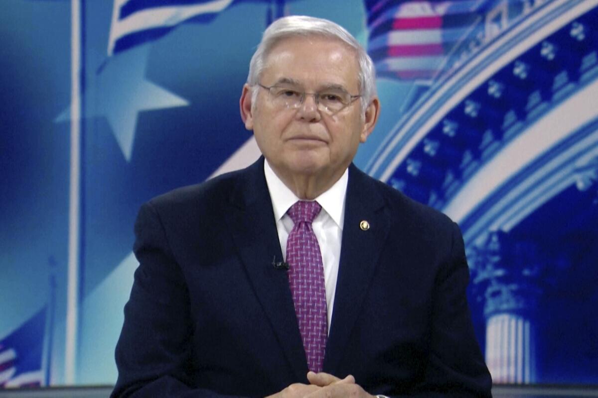 An image from video of Robert Menendez looking into the camera, with a backdrop of patriot images in red, white and blue