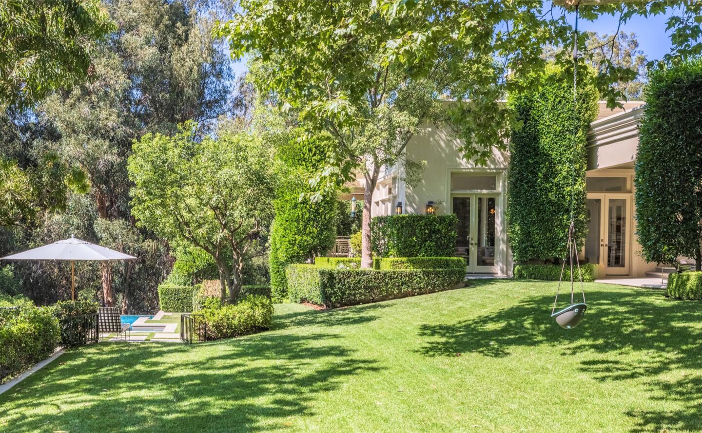 The backyard has a sloping lawn and trees.