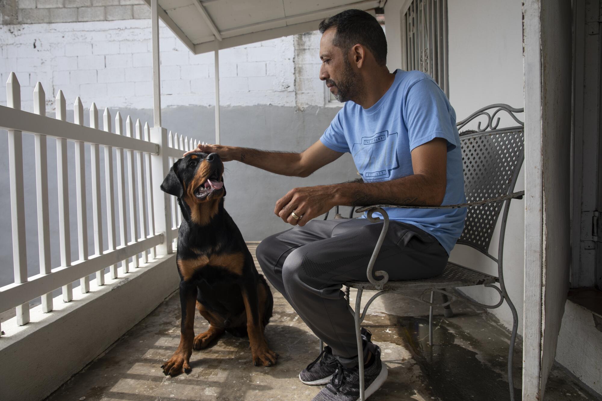 A man on a porch pets a dog