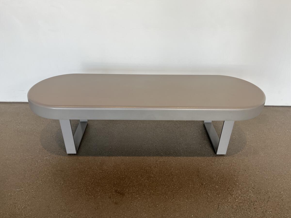 A gray plastic bench on two legs is topped with a seat in the shape of an oval.