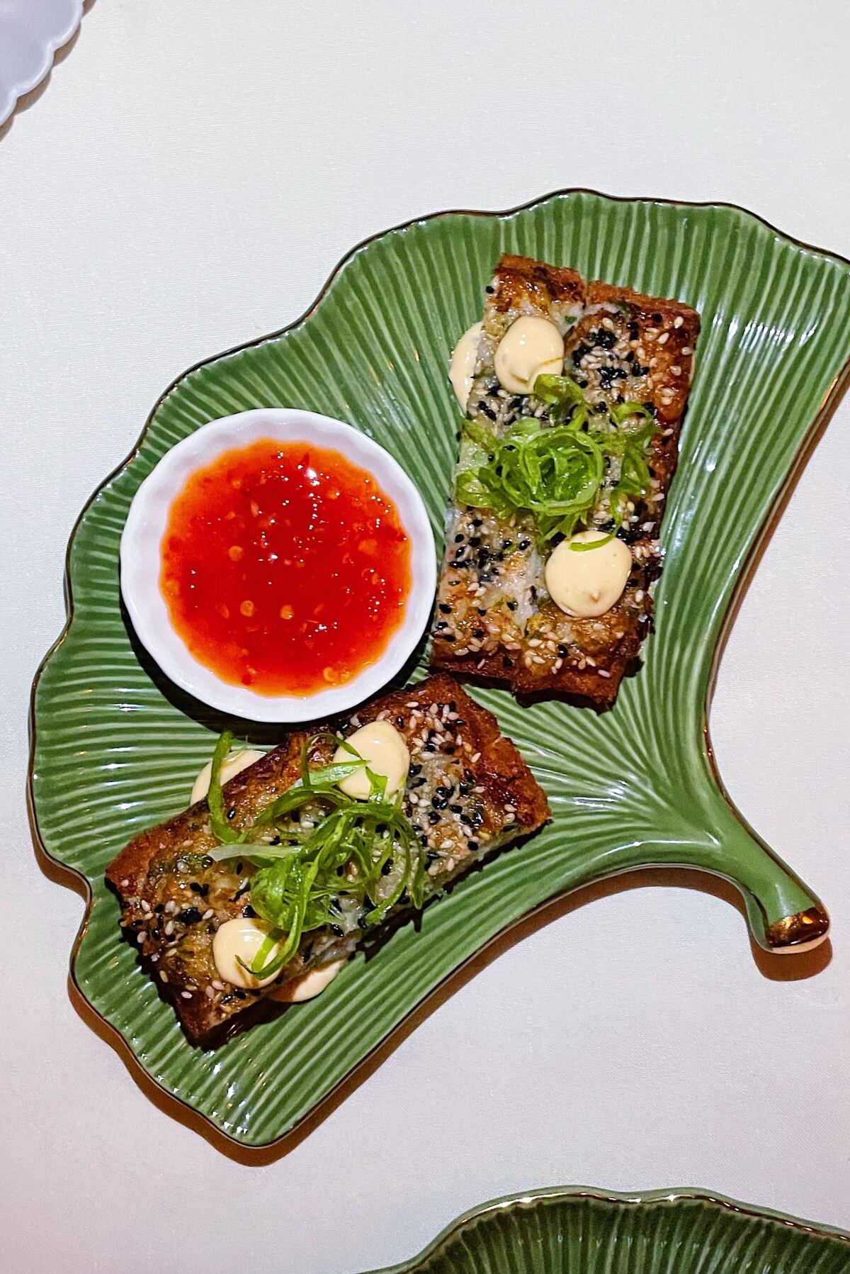 An overhead photo of shrimp toast with red dipping sauce on a green gingko-leaf-shaped plate