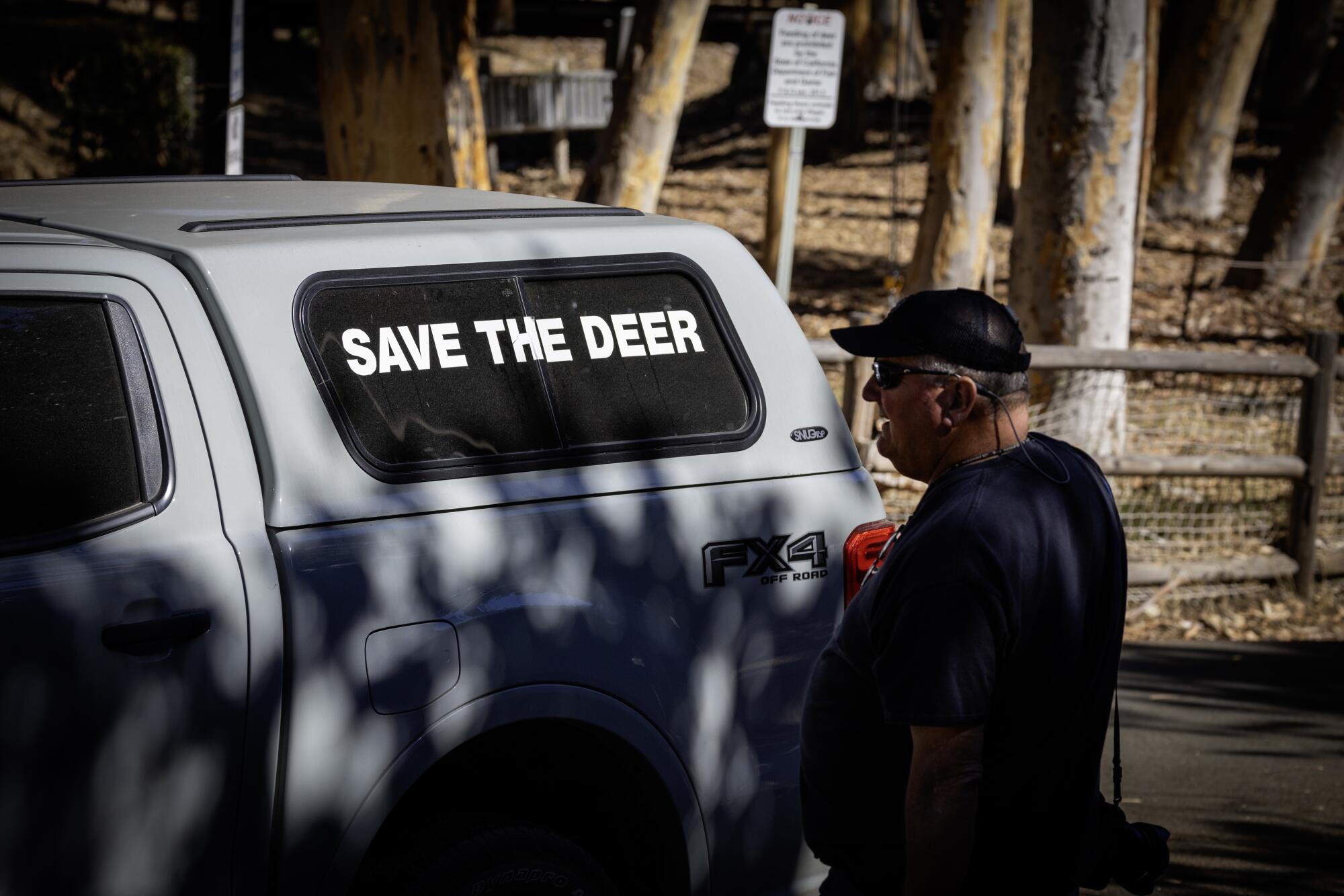 A man stands beside a truck that bears the message "Save the deer."