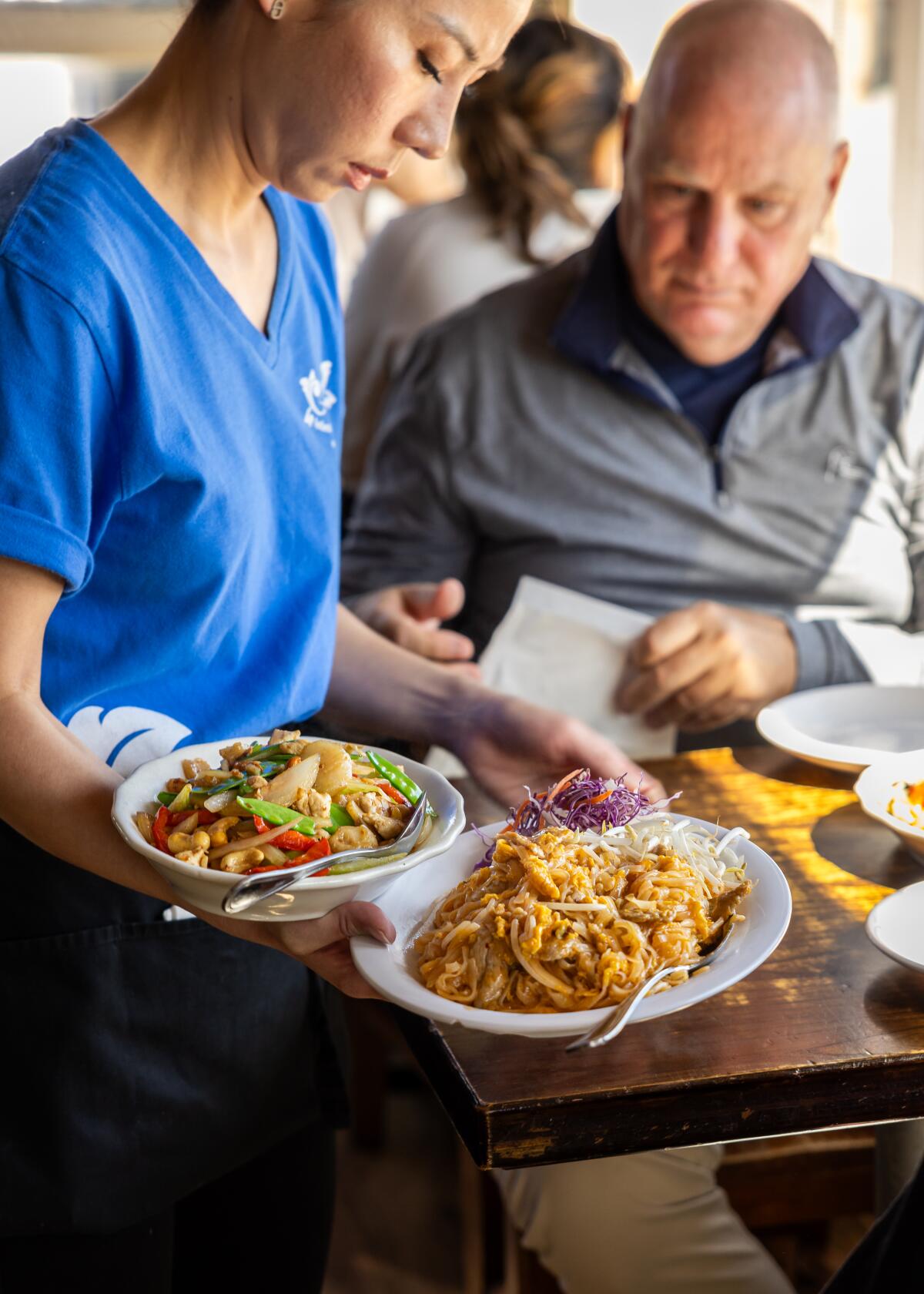A server puts down noodle dishes for seated customer 