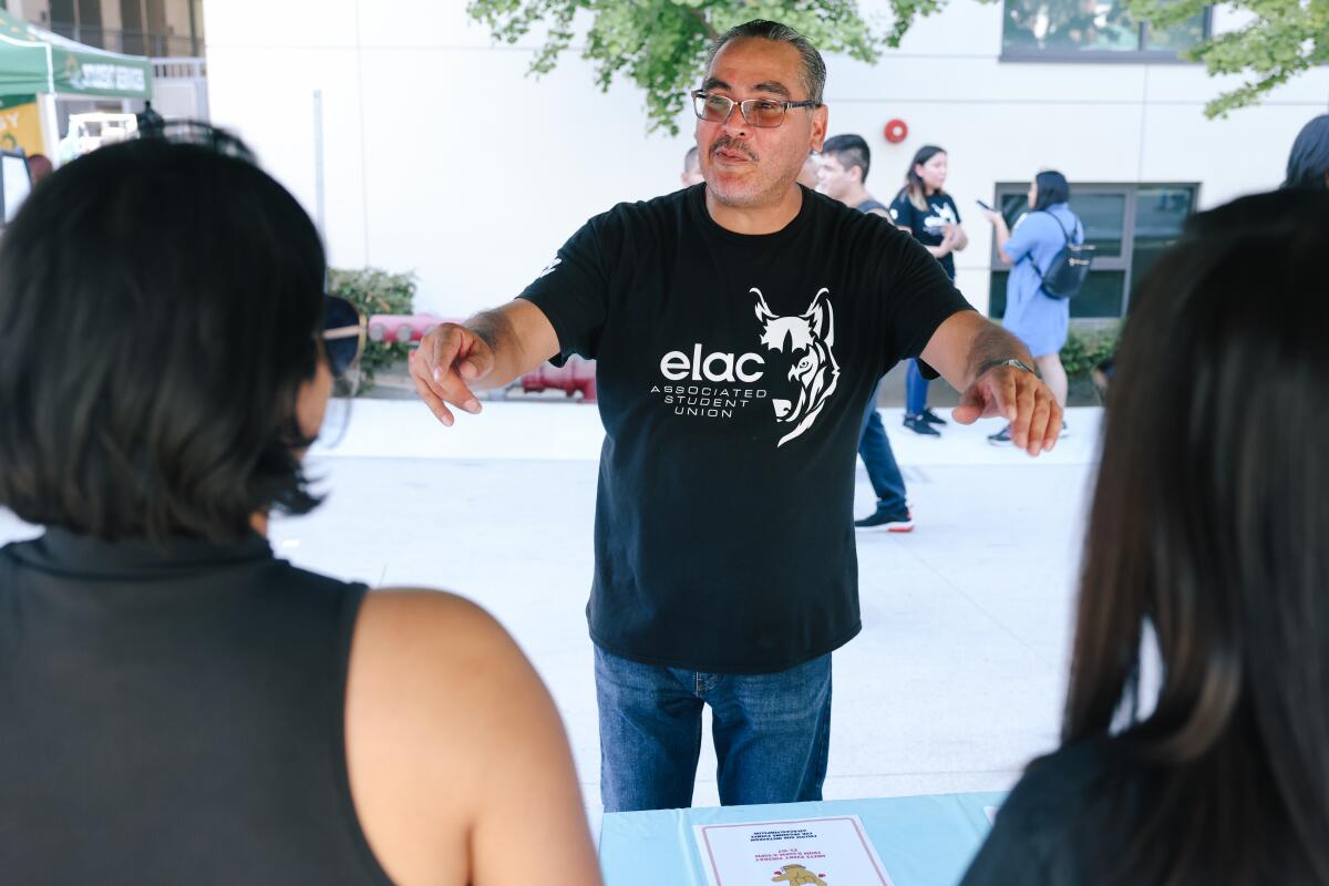 A man wearing an East Los Angeles College T-shirt talks to students on campus. 