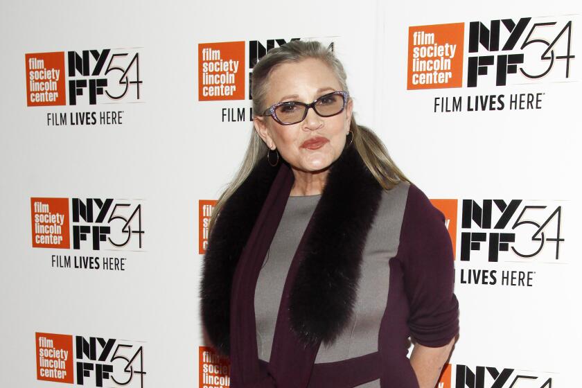 Carrie Fisher wearing tinted glasses, a purple and grey dress and a furry scarf