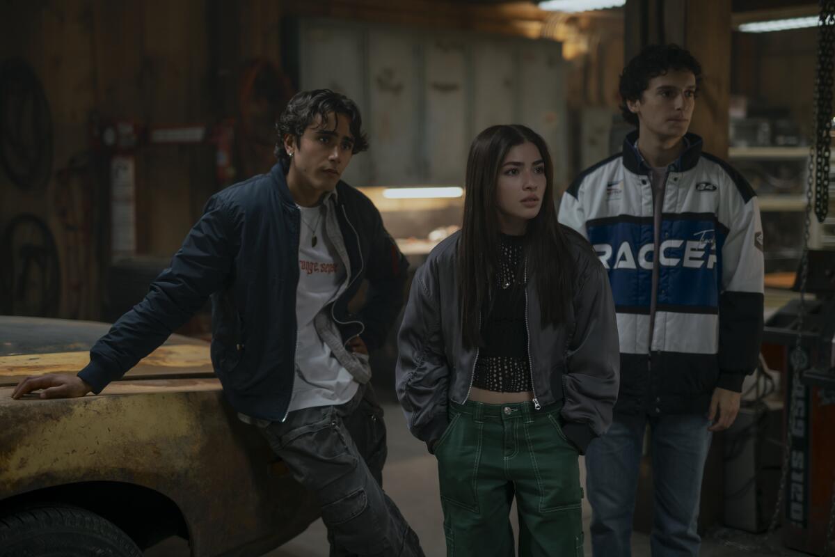 Three teenagers are near a rusty auto in a garage.