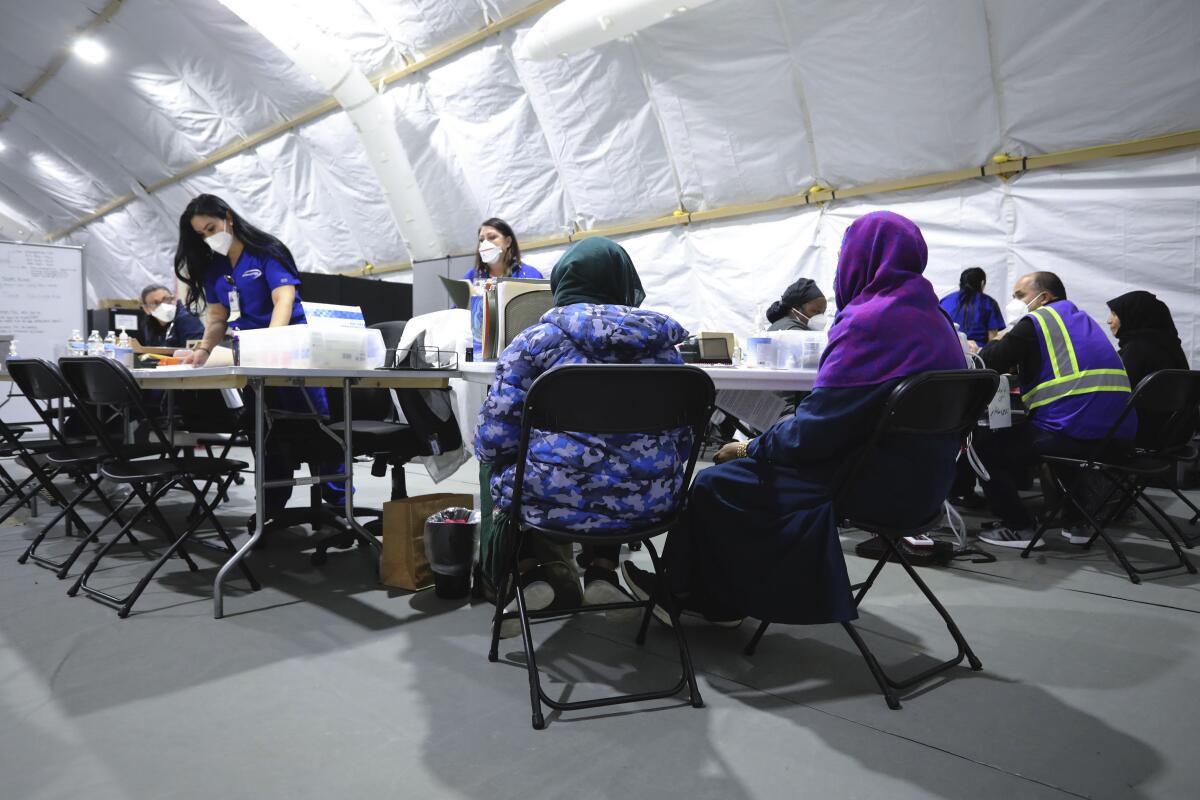 Women seated in folding chairs wait as medical personnel work