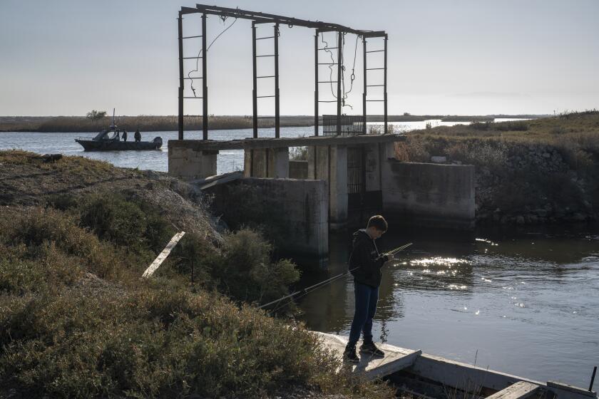 A boy fishes as police border guards on a boat patrol along the Evros River that forms a natural border between Greece and Turkey, on Sunday, Oct. 30, 2022. Greece is planning a major extension of a steel wall along its border with Turkey in 2023, a move that is being applauded by residents in the border area as well as voters more broadly.(AP Photo/Petros Giannakouris)