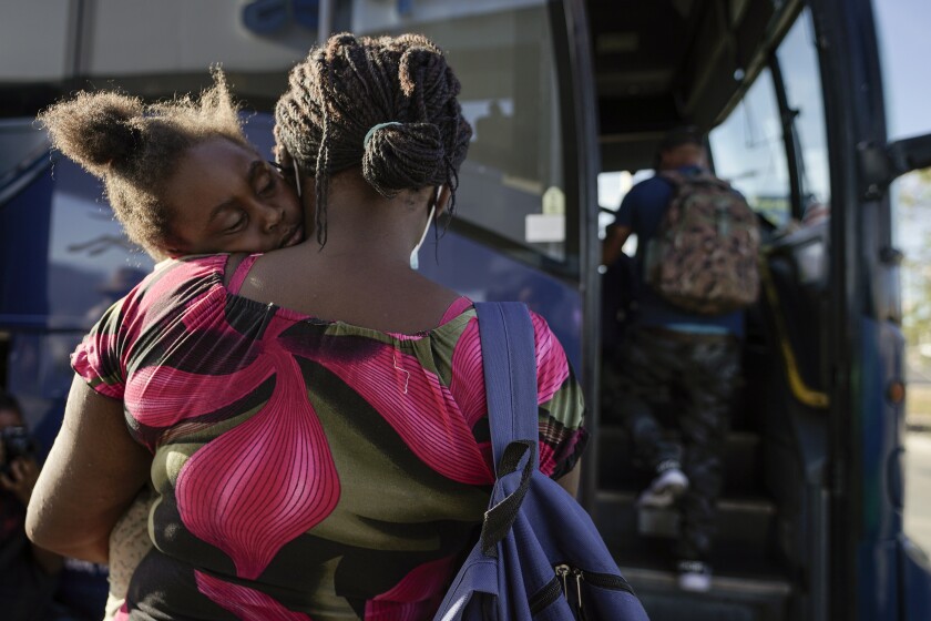 A child sleeps on the shoulder of a woman as they prepare to board a bus