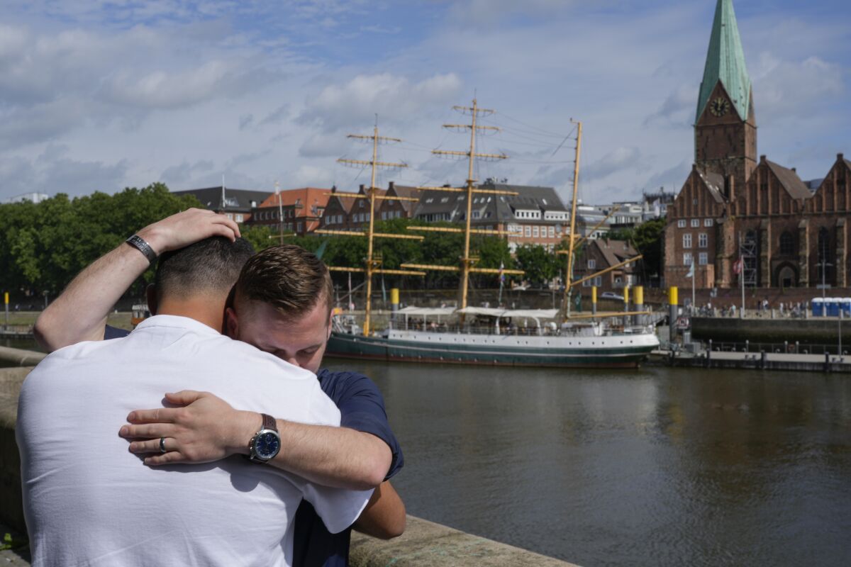 Two men embrace beside a river