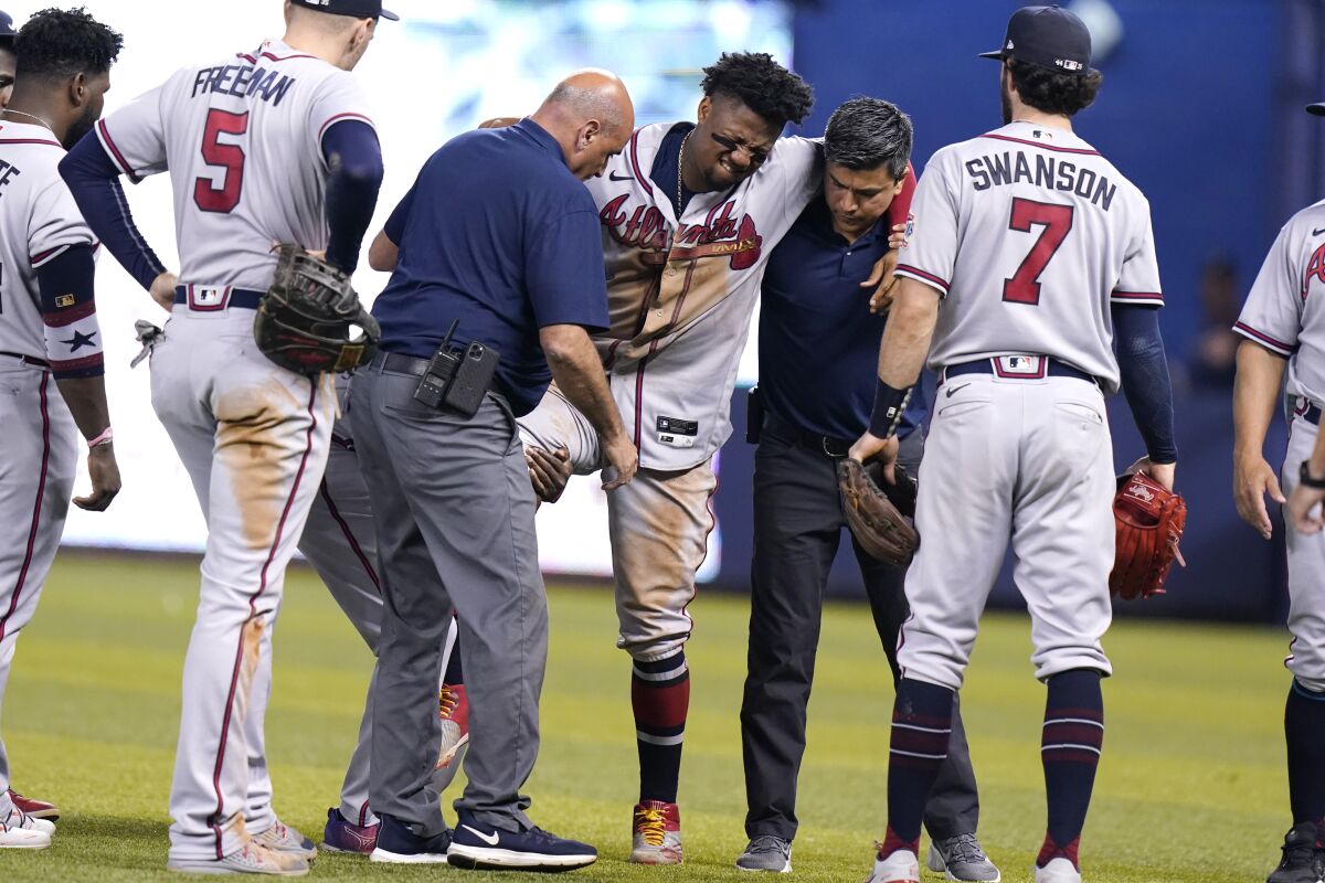Atlanta Braves right fielder Ronald Acuna Jr., center, is carried to a medical cart after trying to make a catch on an inside-the-park home run hit by Miami Marlins' Jazz Chisholm Jr. during the fifth inning of a baseball game, Saturday, July 10, 2021, in Miami. (AP Photo/Lynne Sladky)