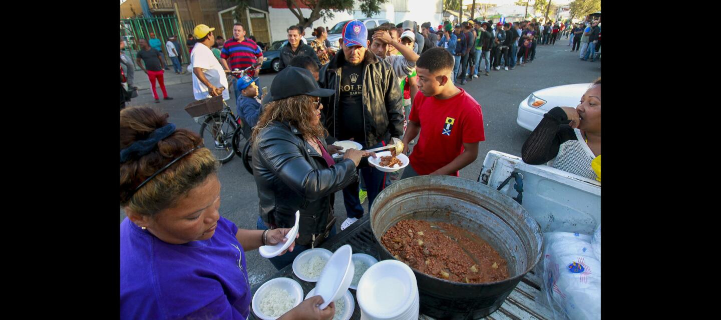 Tijuana resident Isabel Rodriguez pours beans over a bowl of rice while at the back of a pickup truck as she, friends, and family members serve food that they cooked to a long line migrants while outside of the Unidad Deportiva Benito JuÃ¡rez, a sports complex that has been converted to a shelter for migrants, in Tijuana, Mexico on Friday.