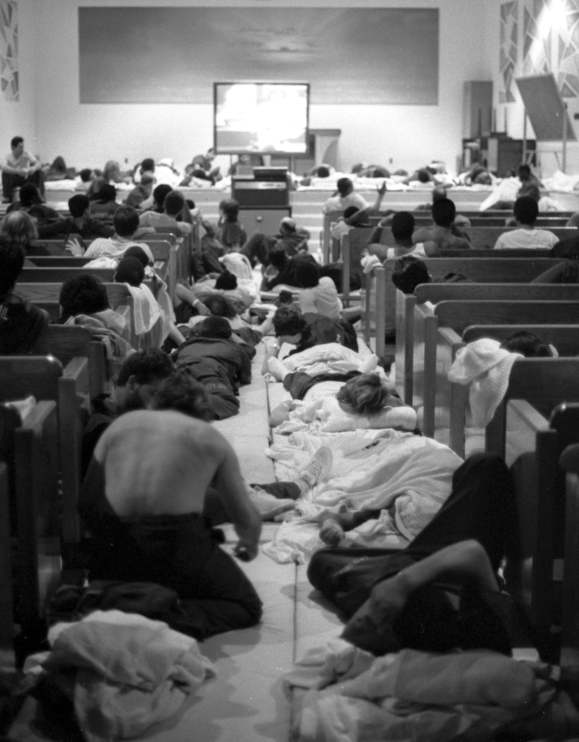 People in a big room sit or lie on the floor and watch a TV.