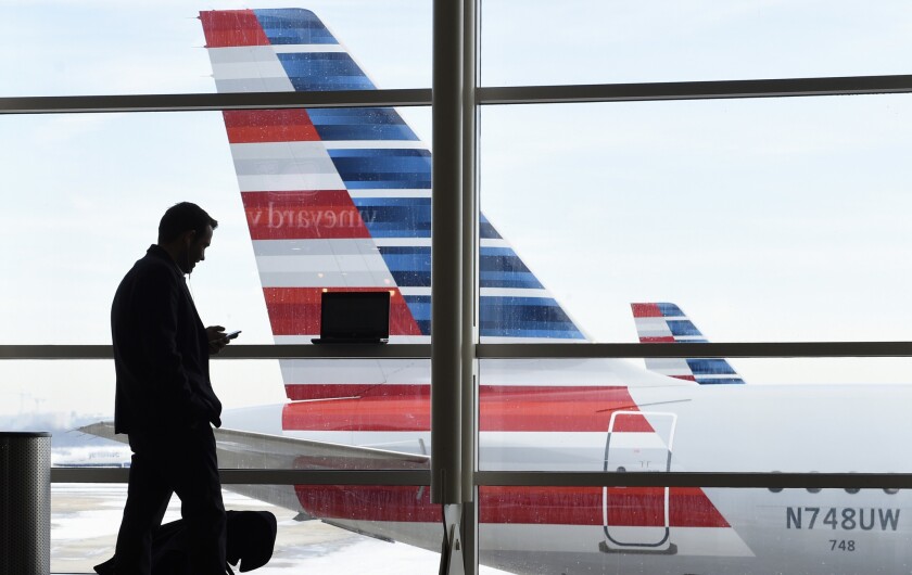 A man looking at his phone is silhouetted in an airport window with passenger jets seen outside