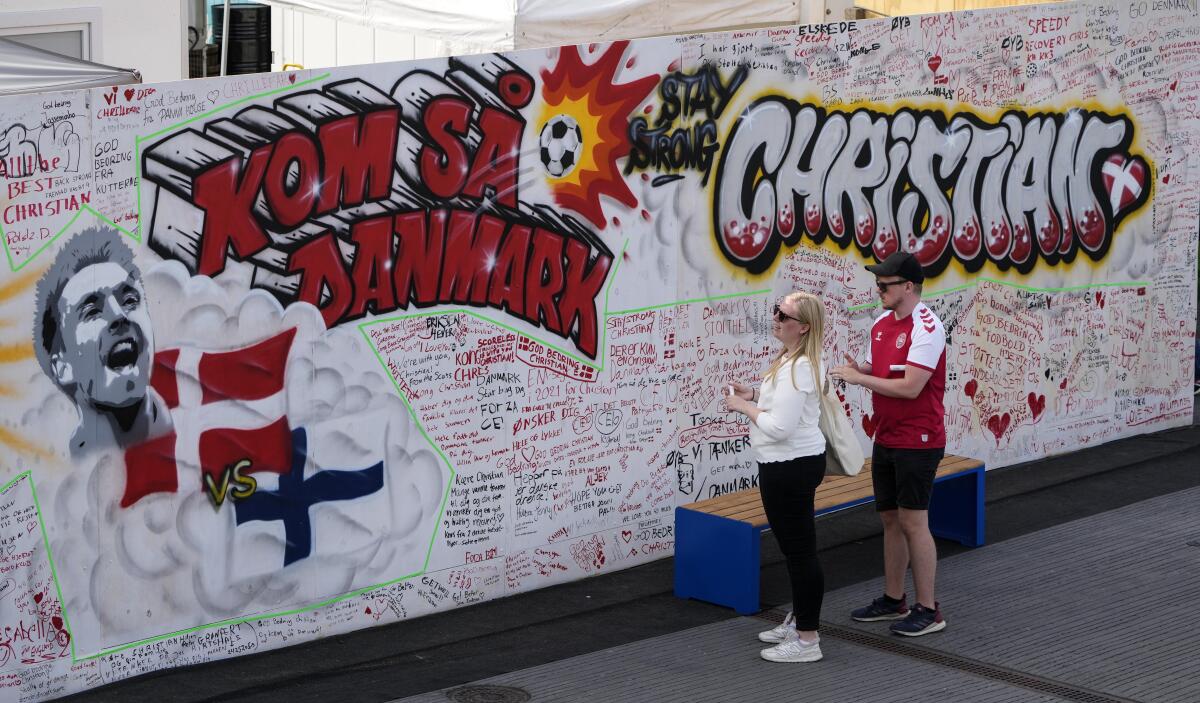 Un par de aficionados escriben mensajes de apoyo junto a un grafiti dedicado al jugador danés Christian Eriksen.