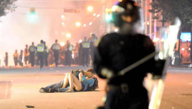 Riot police walk in the street as a couple kiss in Vancouver after riots broke out after game seven.