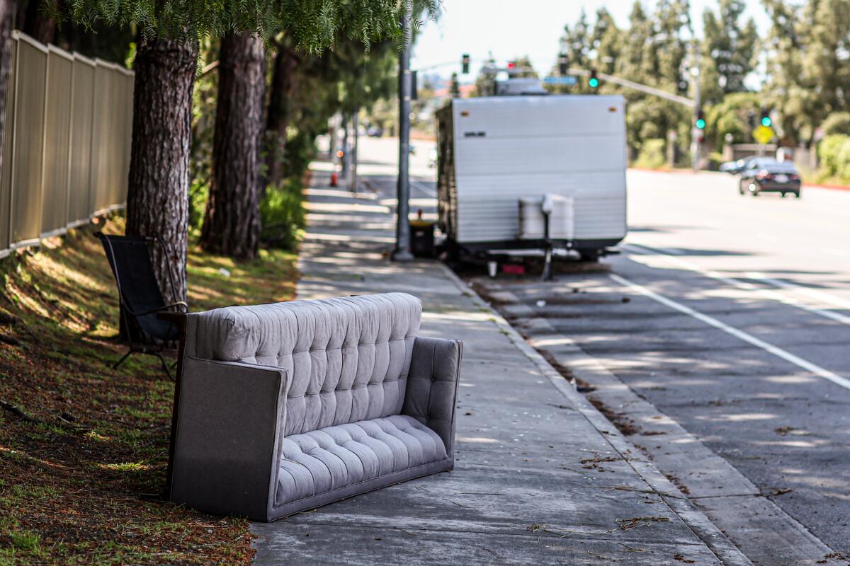 A couch on a sidewalk near an RV.