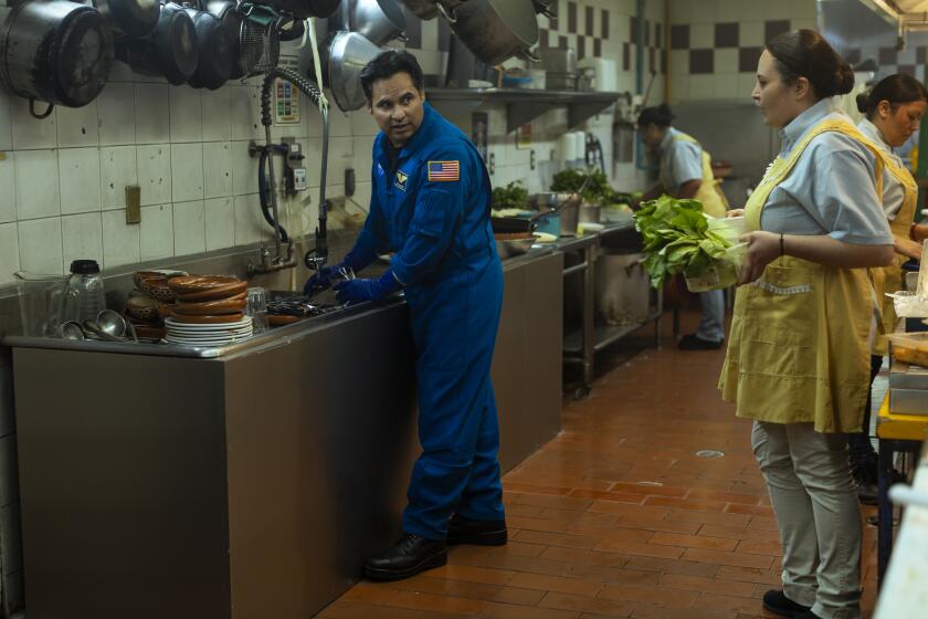 A man in a NASA uniform (Michael Peña as astronaut José M. Hernández) washes dishes in his wife's restaurant.