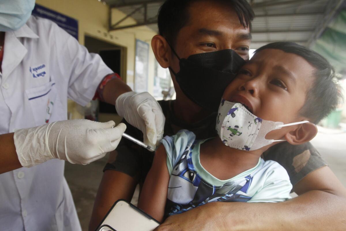 A young boy, held by his father, reacts as he receive a second dose of the Sinovac's COVID-19 vaccine at a Krang Thnung health center outside Phnom Penh, Cambodia, Monday, Nov. 15, 2021. Cambodia reopened its borders to fully vaccinated travelers Monday, two weeks earlier than planned as the country emerges from a lengthy lockdown, bolstered by one of the world's highest rates of immunization against COVID-19. (AP Photo/Heng Sinith)