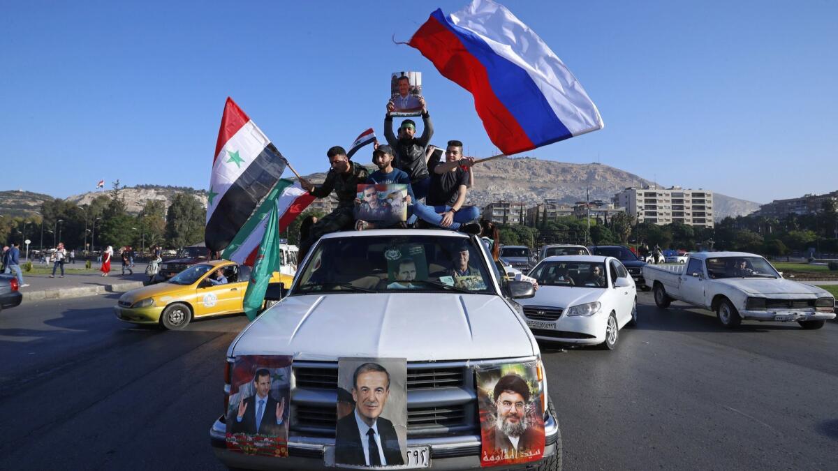 Syrian government supporters wave Syrian, Iranian and Russian flags as they chant slogans against the United States in Damascus on April 14.