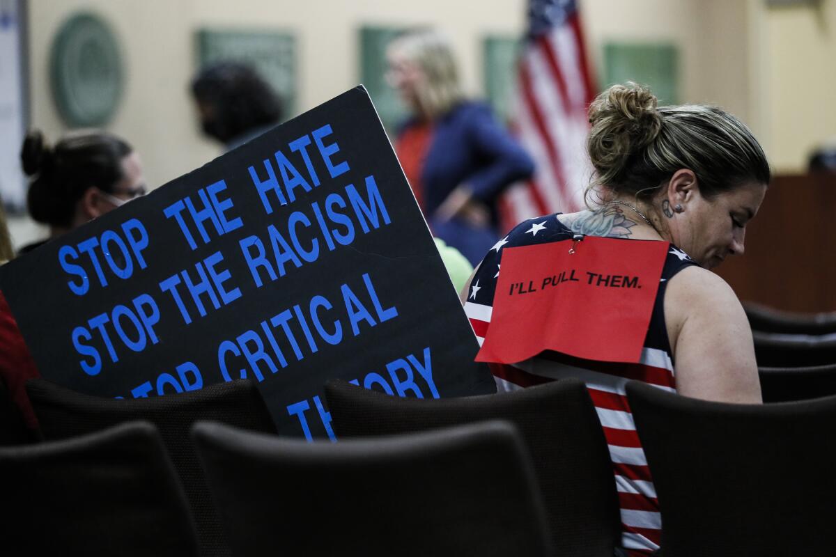 Andria Derio wears a sign stating she will remove her children from the district should the ban not pass.