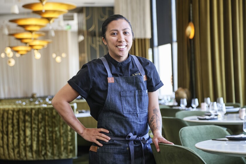 A smiling female executive chef stands in her downtown San Diego restaurant.