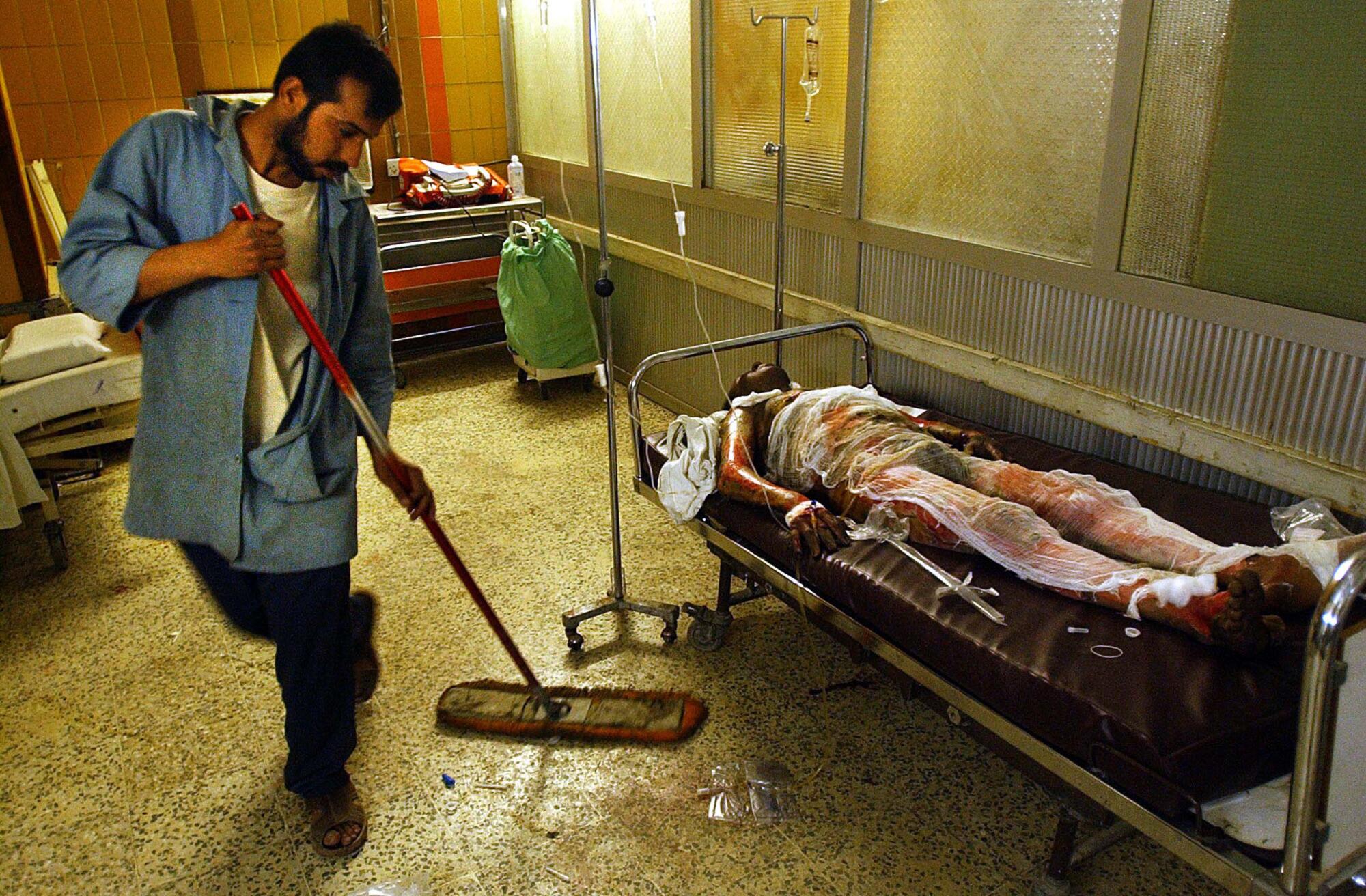 A worker from the Medical City Hospital sweeps the floor next to a burn victim.