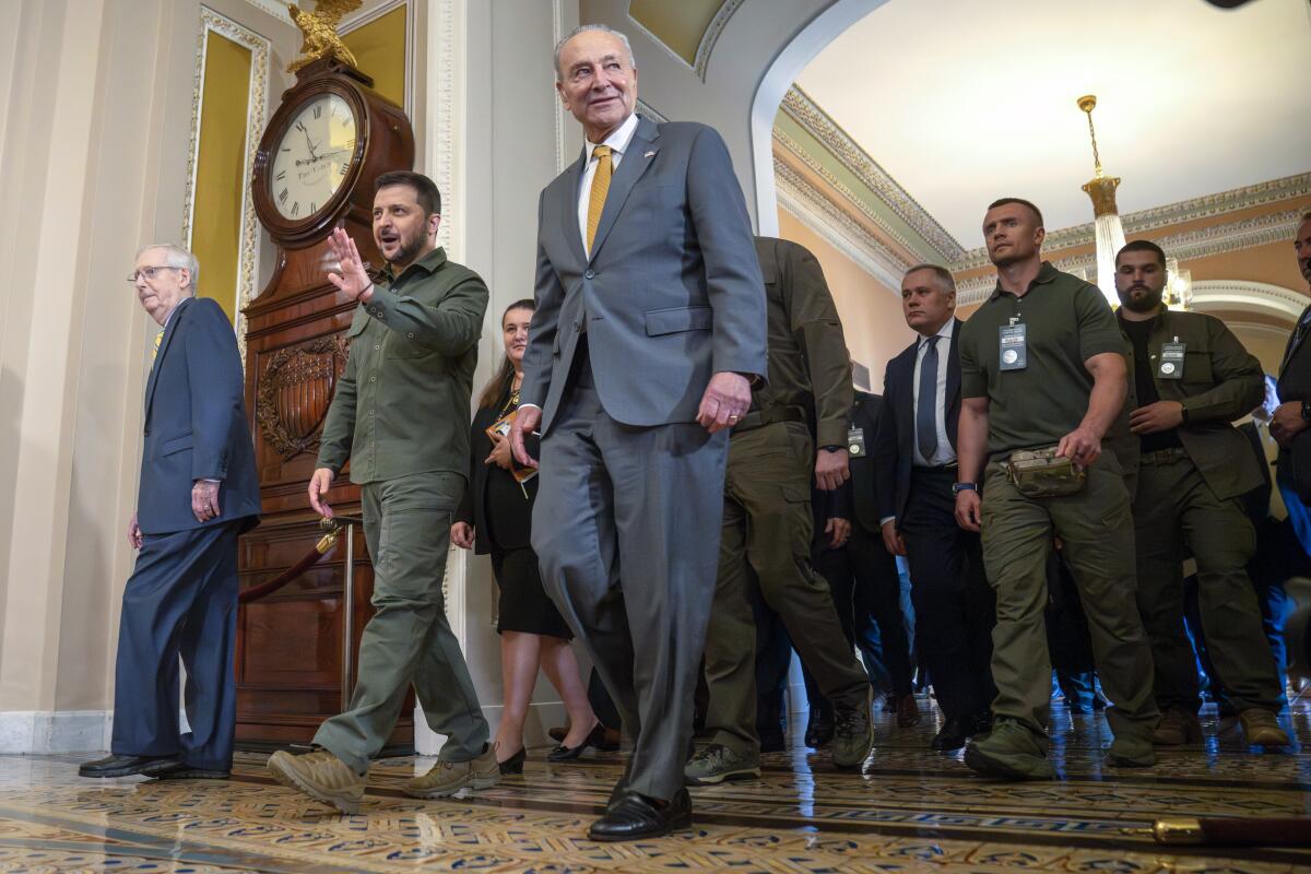 Ukrainian President Volodymyr Zelensky walks with Sens. Mitch McConnell and Charles E. Schumer in an ornate hallway. 
