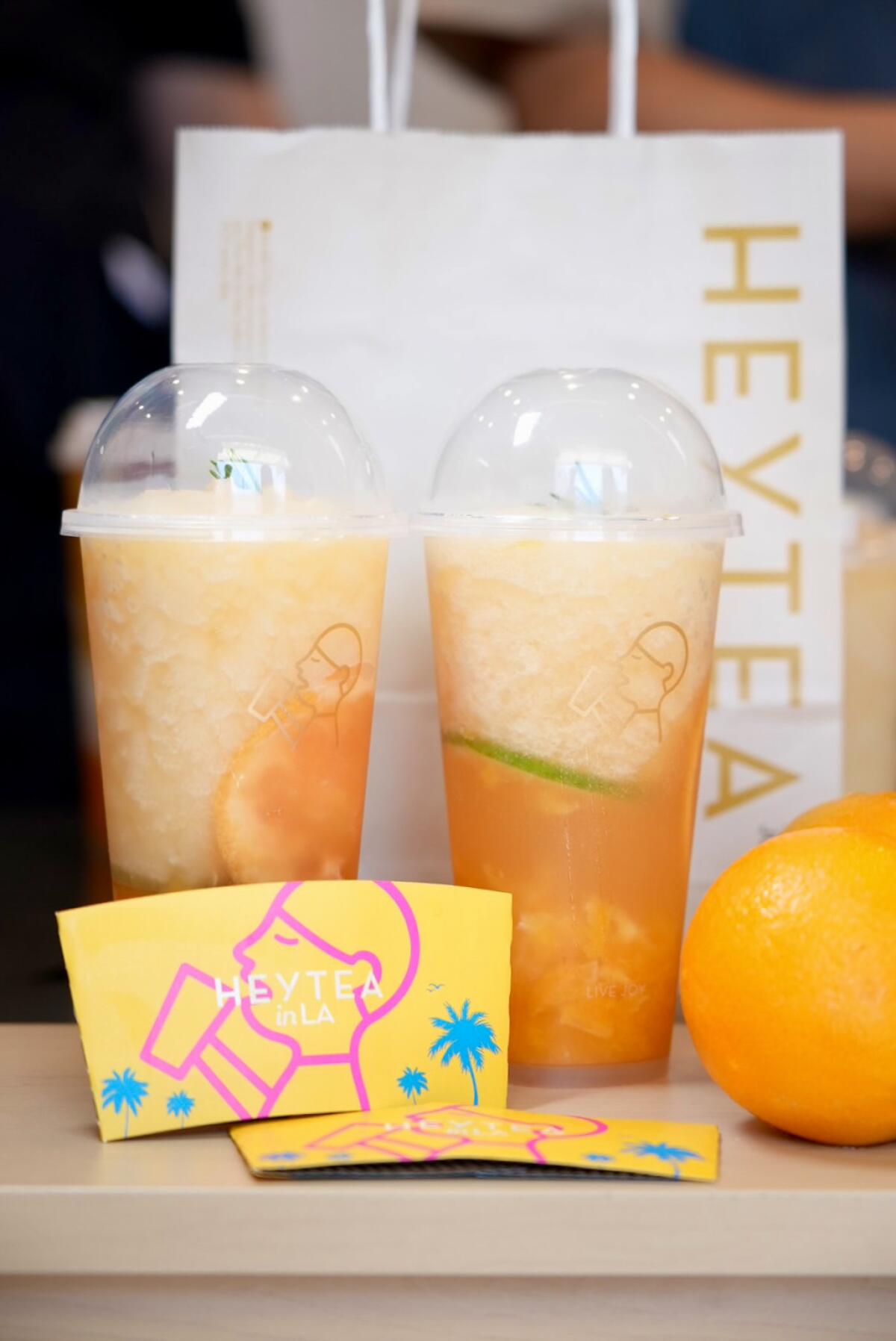 Two cups of an orange drink with a Heytea shopping bag and an orange