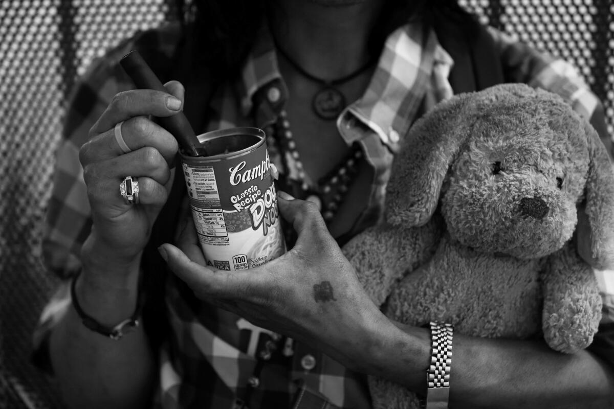 A homeless man eats dinner out of a Campbell's soup can while he clutches a teddy bear at a bus stop on Spring Street.