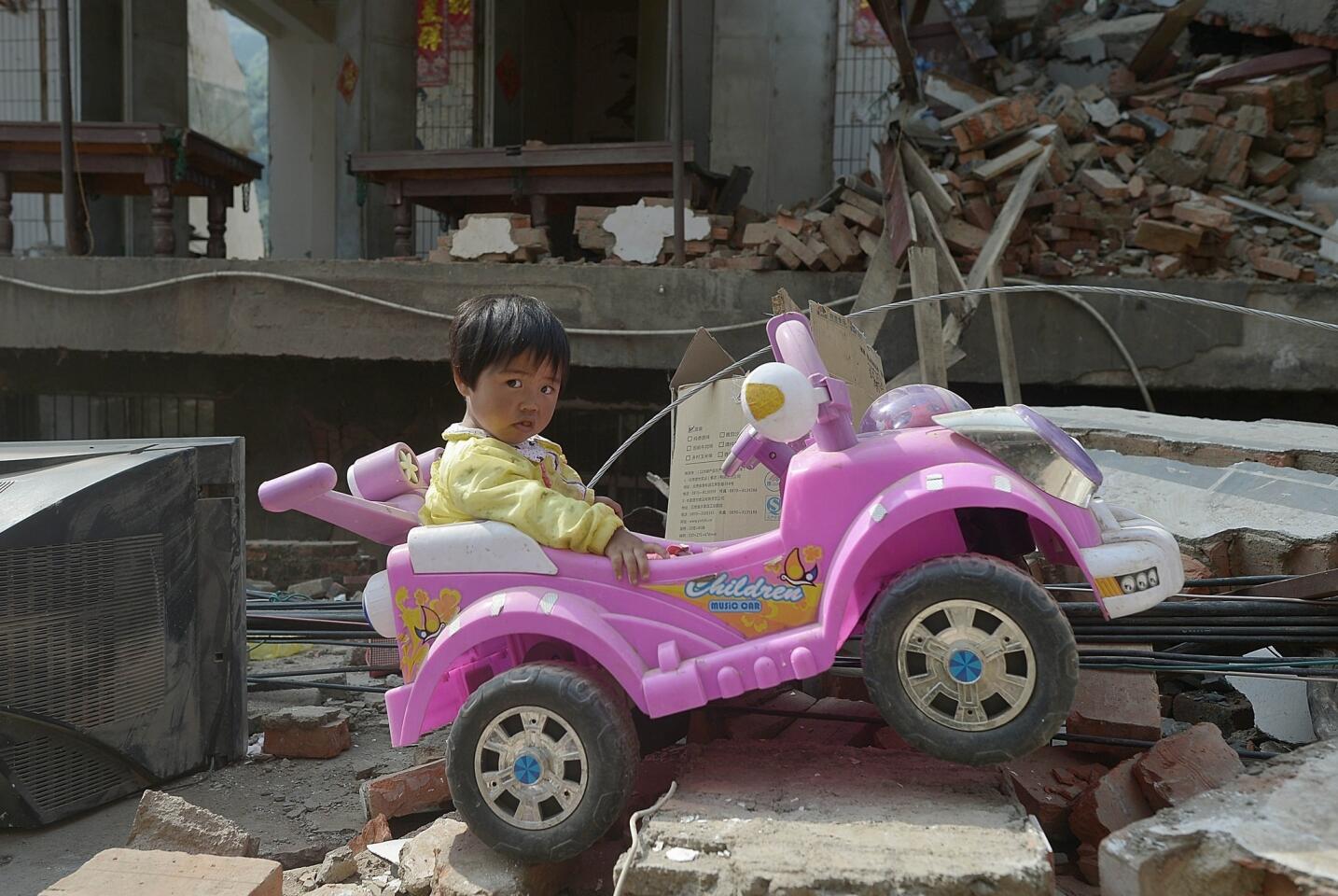 Yan Jiajia, 2, sits on her electric car, which her father dug out of the rubble of their quake-damaged house in Longtoushan township.