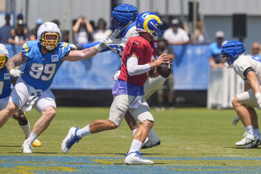 Matthew Stafford, de rojo, quarterback de los Rams de Los Ángeles, corre con el balón durente una práctica conjunta ante los Chargers de Los Ángeles, en The Bolt, en El Segundo, California, el domingo 4 de agosto de 2024. El tackle defensivo de los Chargers Scott Matlock (99) busca presionar a Stafford. (AP Foto/Damian Dovarganes)