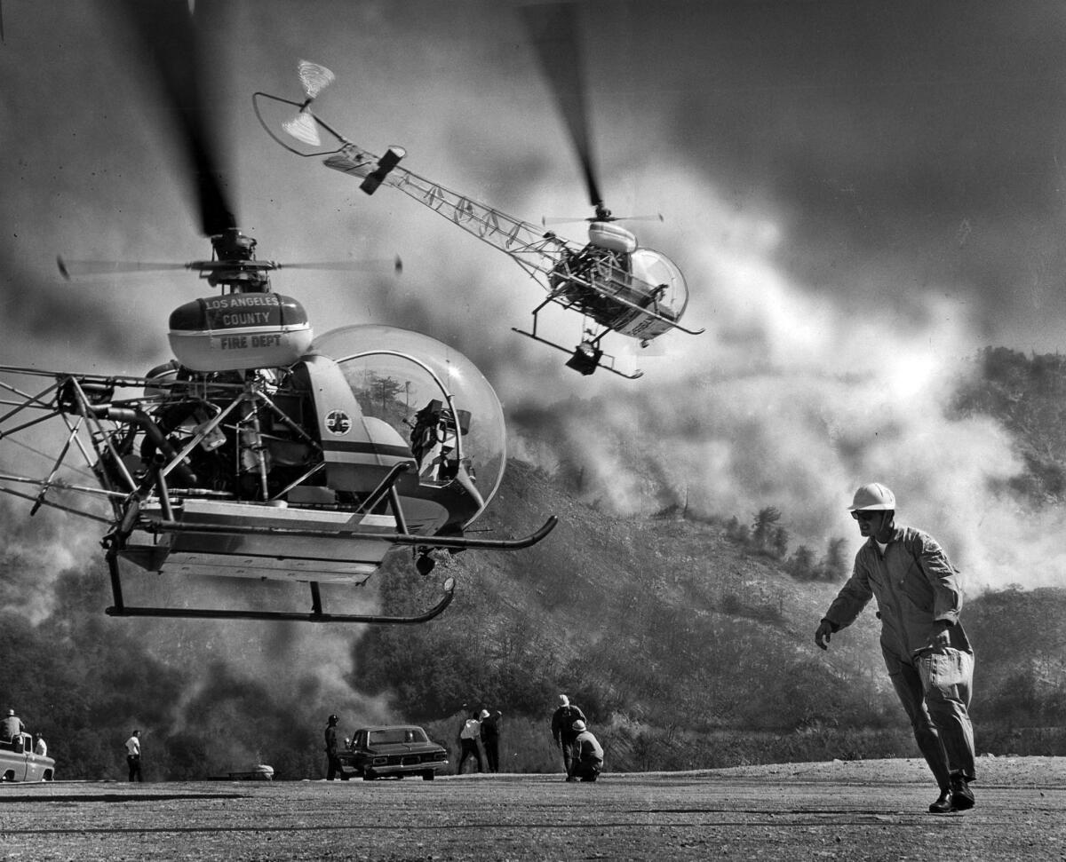 July 16, 1966: Los Angeles County firefighter Earl Wyat, right, directs a water-carrying helicopter off the ground as a brush fire spreads just off Angeles Crest Highway.
