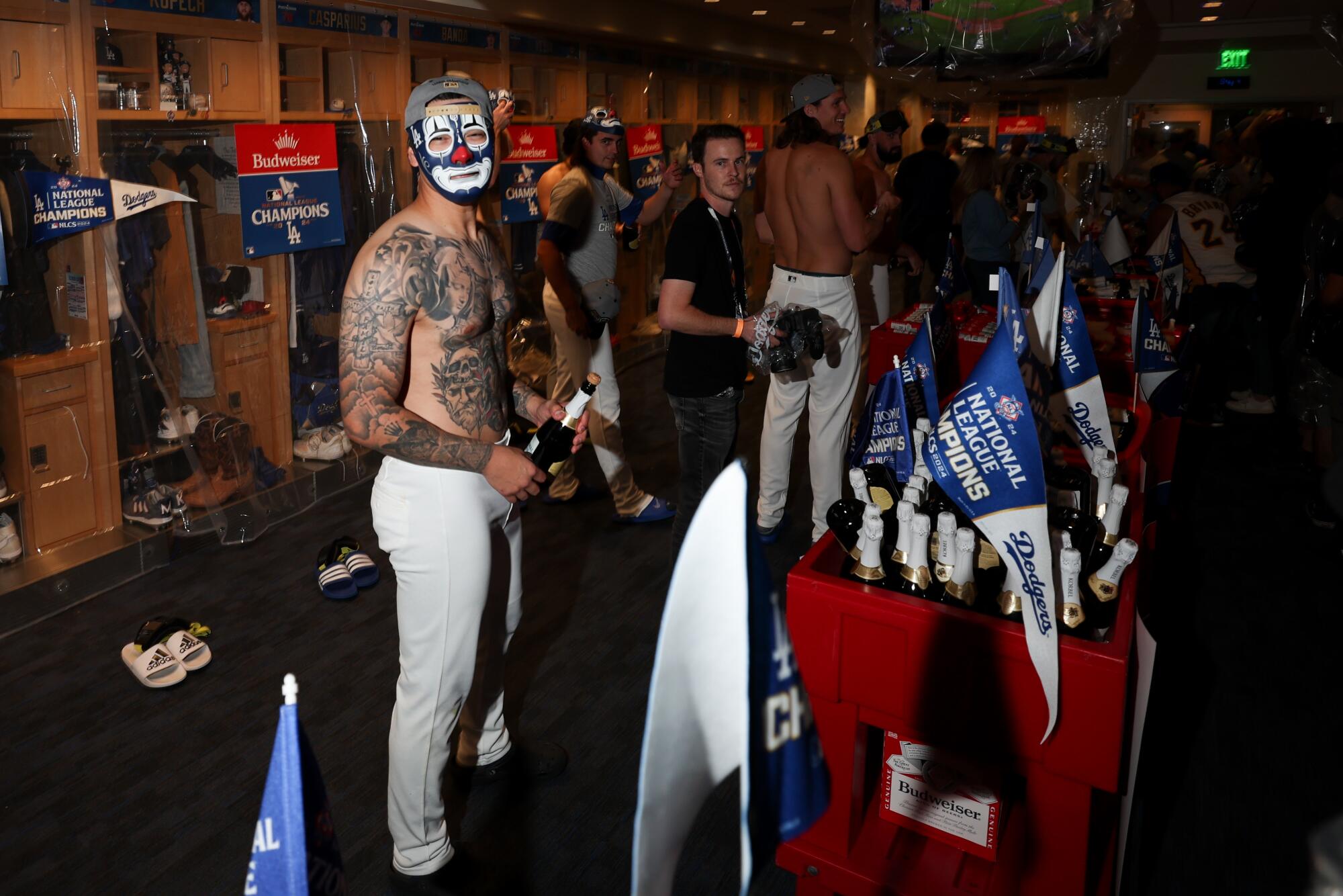 A shirtless Anthony Banda dons a clown mask while holding a champagne bottle in the clubhouse