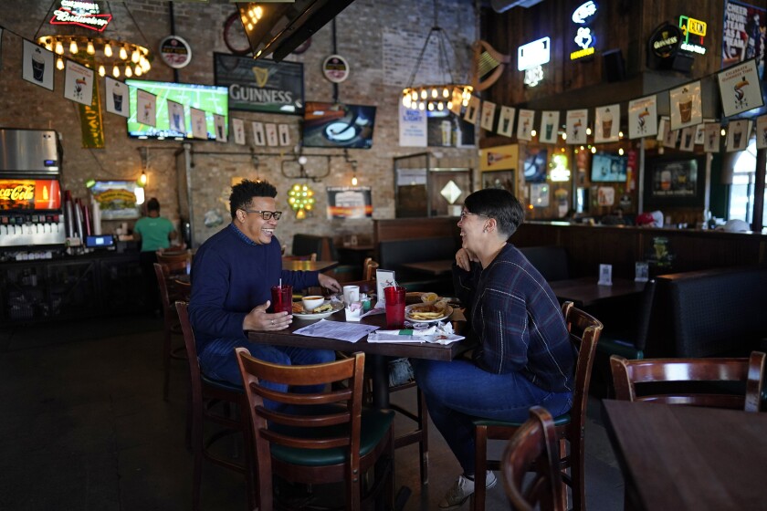 Tasha Arevalo, right, laughs with Joseph Butler while eating at Mo's Irish Pub, Tuesday, March 2, 2021, in Houston. Texas Gov. Greg Abbott announced that he is lifting business capacity limits and the state's mask mandate starting next week. (AP Photo/David J. Phillip)