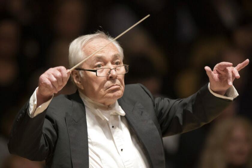 An elderly man conducts an orchestra with his hands in the air