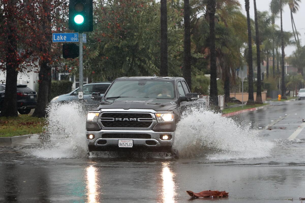 A motorist drives through a large rain puddle at the intersection of Lake Street and Adams Avenue in Huntington Beach.