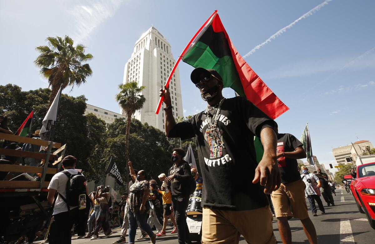 A man in a Black Lives Matter T-shirt and holding a Pan-African flag walks with other people down a city street. 