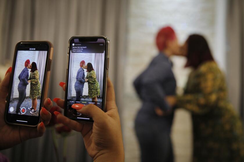 FILE - In this May 8, 2020 file photo, Cynthia Sanchez takes video and pictures as her sister Jennifer Escobar, right, and Luz Sigman kissing during their wedding ceremony at Vegas Weddings in Las Vegas. Las Vegas has been known for decades as the place for exuberant nuptials blessed by the swirl of Elvis' white capes. But for years legal marriages were barred for same-sex couples. Now, the state that's home to the self-proclaimed "wedding capital of the world" is the first in the country to officially protect same-sex marriage in its constitution. (AP Photo/John Locher, File)