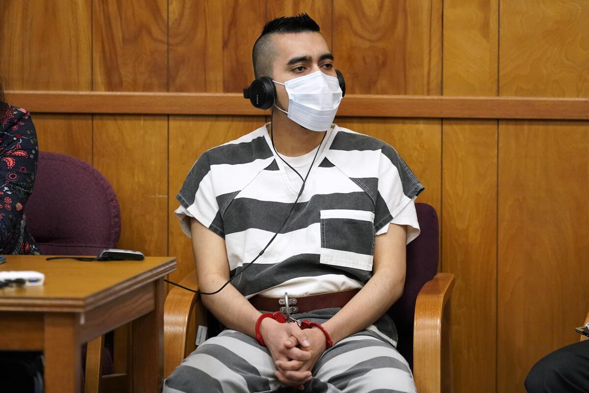 A man in prison garb, headphones and a mask sits in a chair.