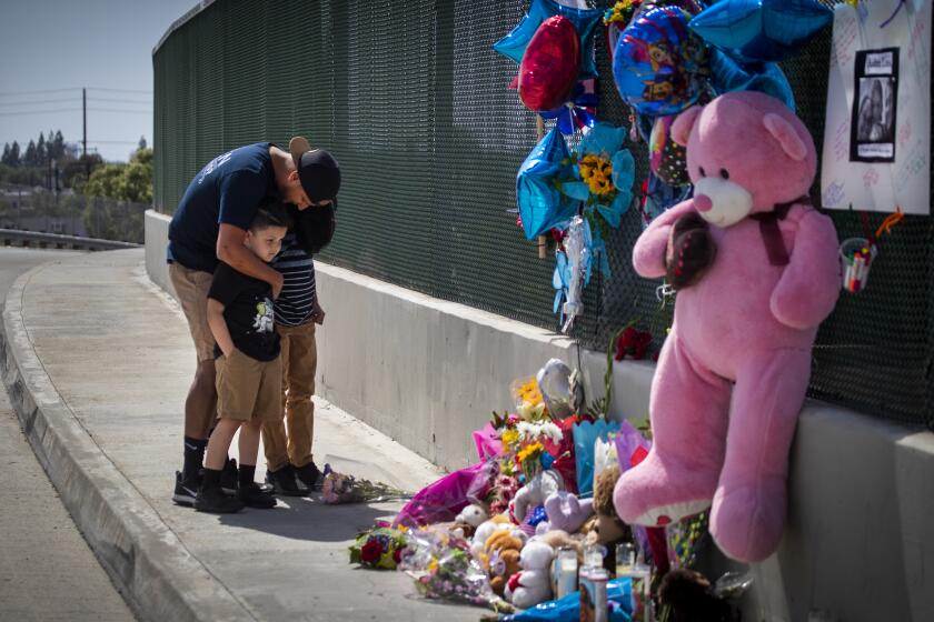 Orange, CA - May 22: George Aguilar prays with his sons, Jackson, 7, and Jacob, 11, of Anaheim, as they place flowers on a growing memorial on the Walnut Ave. overpass of the 55 Freeway, where 6-year-old boy died after being shot in an apparent road-rage incident Friday morning on the northbound 55 Freeway near the Chapman Ave. exit in 55 Freeway on Saturday, May 22, 2021 in Orange, CA. "I wanted to pay my respects and bring flowers, said Aguilar. "That could have been one of my kids." The gunman and accomplice remain at large. Officials are searching for a newer white sedan, possibly a "Volkswagen wagon sedan," that fled north on the 55 Freeway, (Allen J. Schaben / Los Angeles Times)