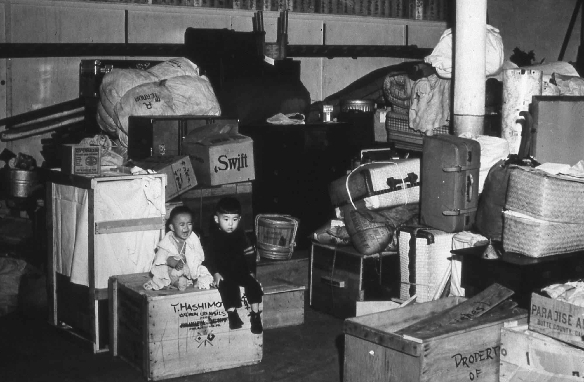 A girl in tears and a boy sit amid the boxes and suitcases of people of Japanese ancestry who were incarcerated in 1942. 