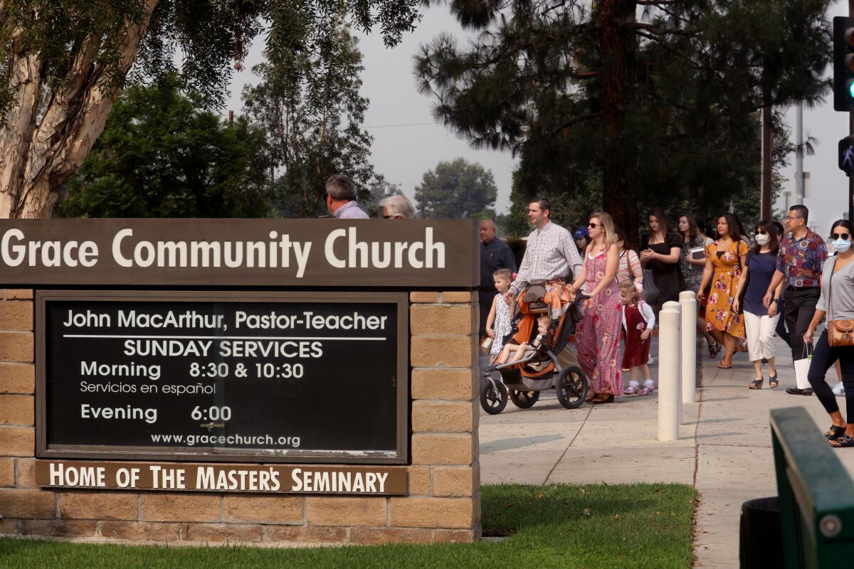 People, only a few wearing masks, walk past a sign into the entrance of Grace Community Church