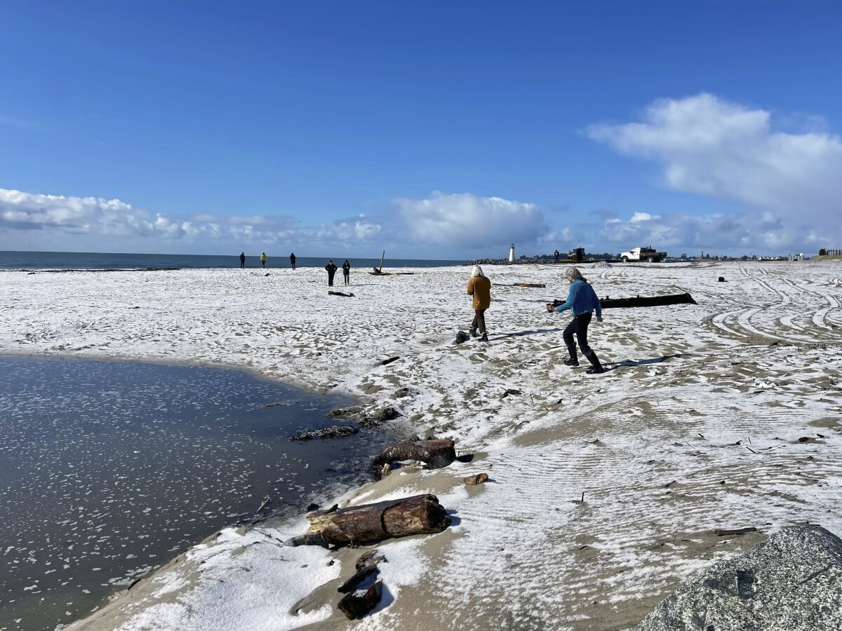 People walk along a snow-covered Twin Lakes State Beach in Santa Cruz.
